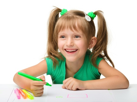 Cute little girl draws with markers while sitting at table, isolated over whiteの写真素材