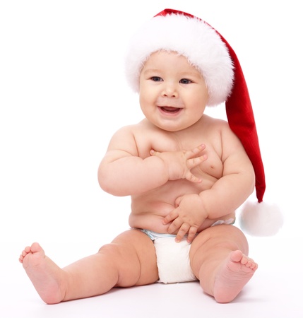 Adorable child is sitting on floor, wearing red Christmas cap, isolated over whiteの写真素材