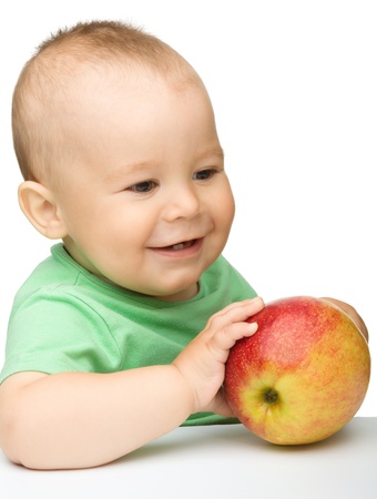 Cute little child is biting red apple while sitting at table, isolated over whiteの写真素材
