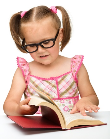 Cute little girl wearing glasses is flipping over pages of a book, isolated on whiteの写真素材