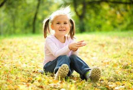 Little girl is sitting on green meadow holding her head with handsの写真素材
