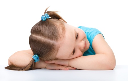 Little girl is sleeping at table laying her head on hands, isolated over whiteの写真素材