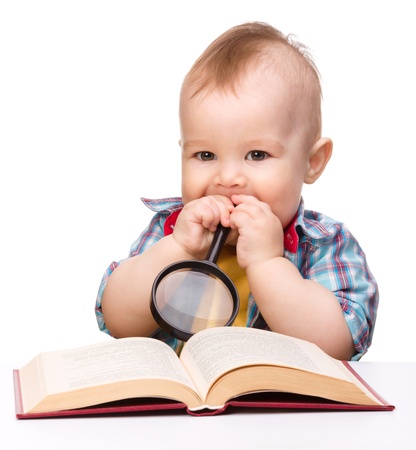 Cute little child play with book and magnifier while sitting at table, isolated over whiteの写真素材