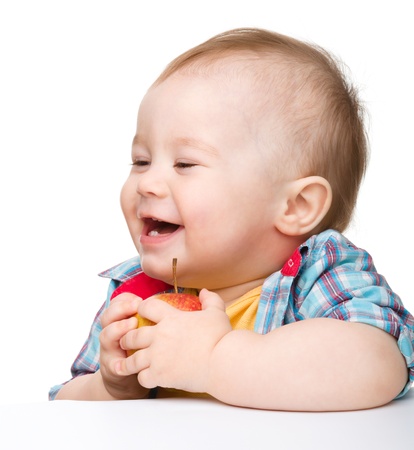 Cute little child is eating red apple and smile while sitting at table, isolated over whiteの写真素材