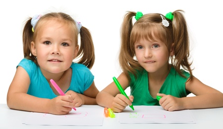 Two little girls draw with markers while sitting at table, isolated over whiteの写真素材