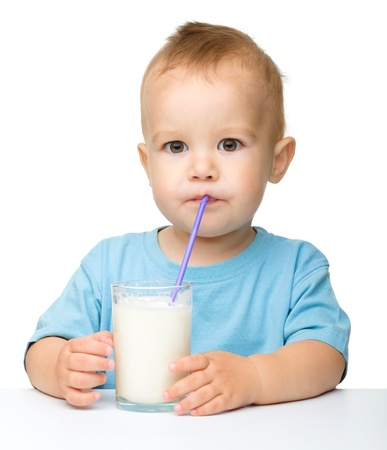 Cute little boy is drinking milk using straw while sitting at table, isolated over whiteの写真素材