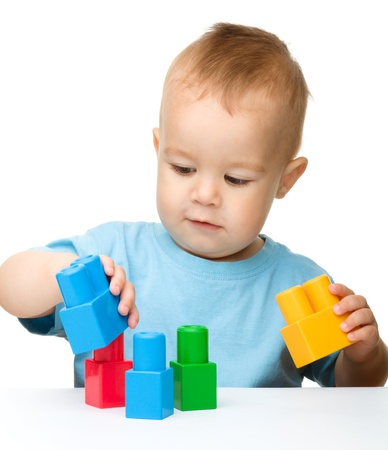 Cute little boy is playing with building bricks while sitting at the table, isolated over whiteの写真素材