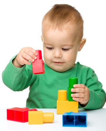 Cute little boy is playing with building bricks while sitting at the table, isolated over whiteの写真素材