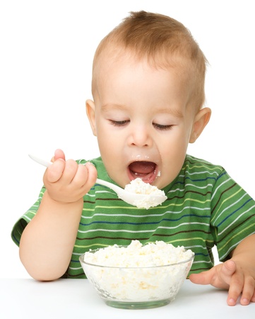 Cute little boy is eating cottage cheese using spoon, isolated over whiteの写真素材