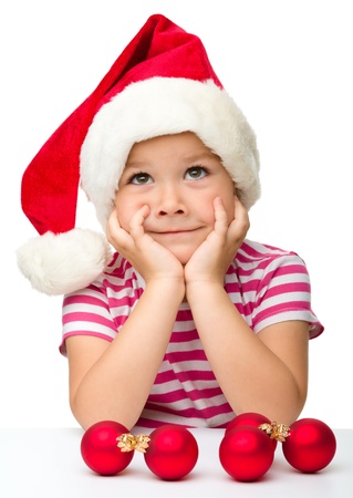 Cute little girl is sitting at table wearing santa hat, isolated over whiteの写真素材