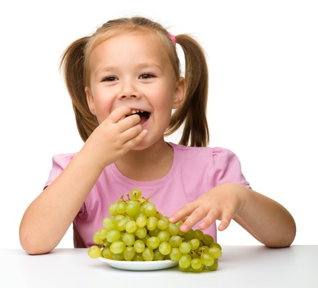 Little girl is eating grapes, isolated over whiteの写真素材