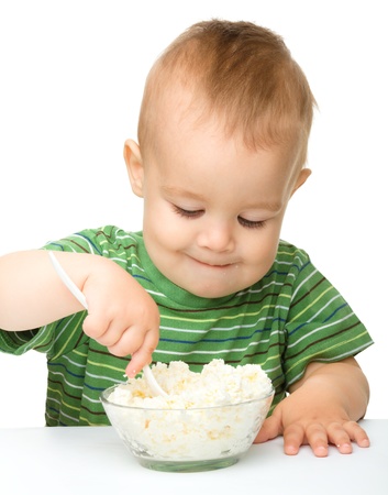 Cute little boy is eating cottage cheese using spoon, isolated over whiteの写真素材