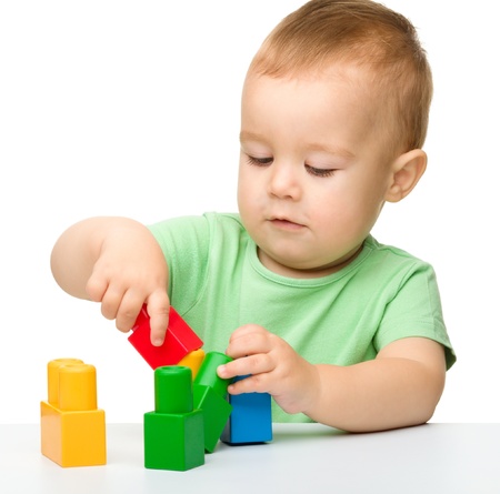 Cute little boy is playing with building bricks while sitting at the table, isolated over whiteの写真素材