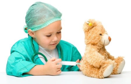 Cute little girl is playing doctor with syringe and teddy bear, isolated over whiteの写真素材