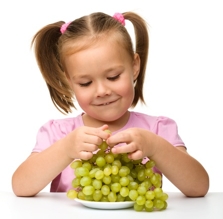 Little girl is eating grapes, isolated over whiteの写真素材