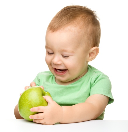 Cute little child is eating green apple while sitting at table, isolated over whiteの写真素材
