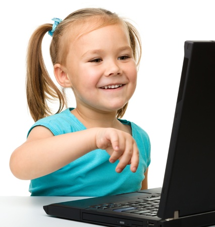 Cute little girl is sitting at table with her black laptop, isolated over whiteの写真素材