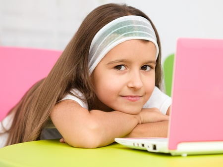 Cute little girl is sitting at table with her pink laptopの写真素材