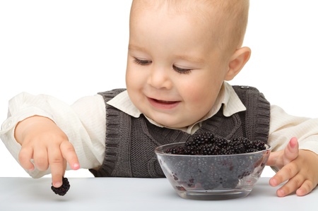 Cute little boy is eating blackberry, isolated over whiteの写真素材