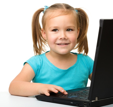 Cute little girl is sitting at table with her black laptop, isolated over whiteの写真素材