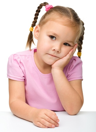 Portrait of a sad little girl sitting at table, isolated over whiteの写真素材