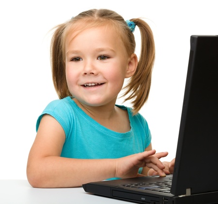 Cute little girl is sitting at table with her black laptop, isolated over whiteの写真素材