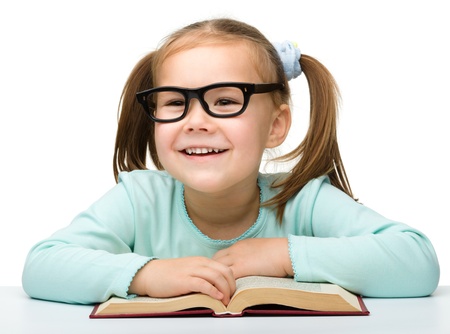 Cute little girl reads a book while wearing glasses, isolated over whiteの写真素材