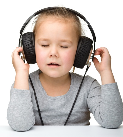 Cute little girl enjoying music using headphones, isolated over whiteの写真素材