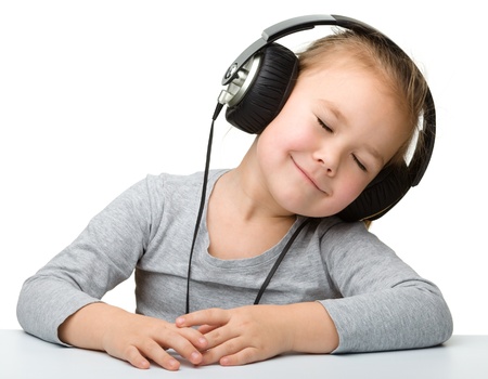 Cute little girl enjoying music using headphones, isolated over whiteの写真素材