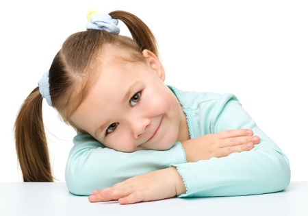 Portrait of a cute little girl sitting at table, isolated over whiteの写真素材