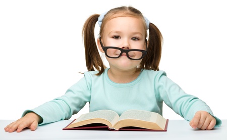 Cute little girl reads a book while wearing glasses, isolated over whiteの写真素材