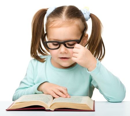 Cute little girl reads a book while wearing glasses, isolated over whiteの写真素材