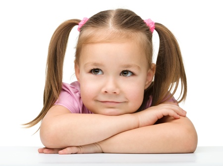 Portrait of a cute little girl sitting at table, isolated over whiteの写真素材