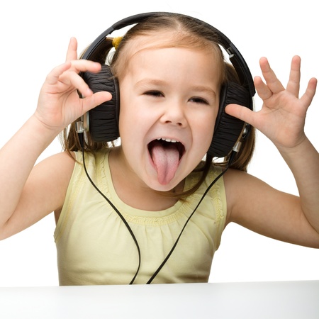 Cute little girl enjoying music using headphones and showing her tongue, isolated over whiteの写真素材