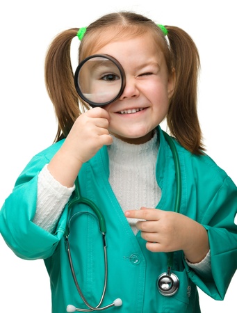 Cute little girl is playing doctor looking through magnifier, isolated over whiteの写真素材