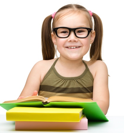 Cute little girl reads a book while wearing glasses, isolated over whiteの写真素材