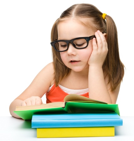 Cute cheerful little girl reading book wearing glasses, isolated over whiteの写真素材