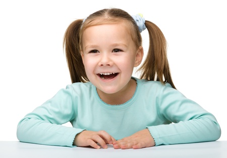 Happy little girl sits at a table and smile, isolated over whiteの写真素材