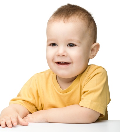 Portrait of a cute cheerful little boy, who is smiling while sitting at table, isolated over whiteの写真素材