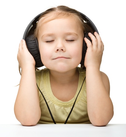 Cute little girl enjoying music using headphones, isolated over whiteの写真素材