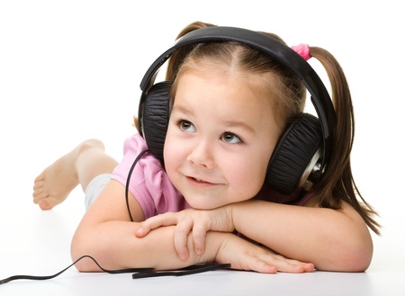 Cute little girl enjoying music using headphones, isolated over whiteの写真素材