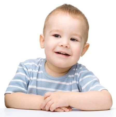 Portrait of a cute cheerful little boy, who is smiling while sitting at table, isolated over whiteの写真素材