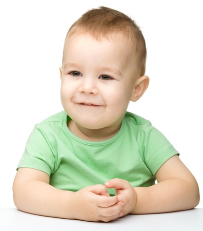 Portrait of a cute cheerful little boy, who is smiling while sitting at table, isolated over whiteの写真素材