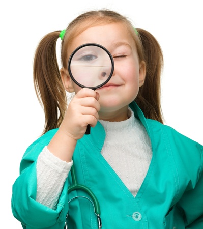 Cute little girl is playing doctor looking through magnifier, isolated over whiteの写真素材