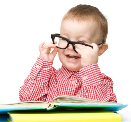 Cute little child play with book while sitting at table and wearing glasses, isolated over whiteの写真素材