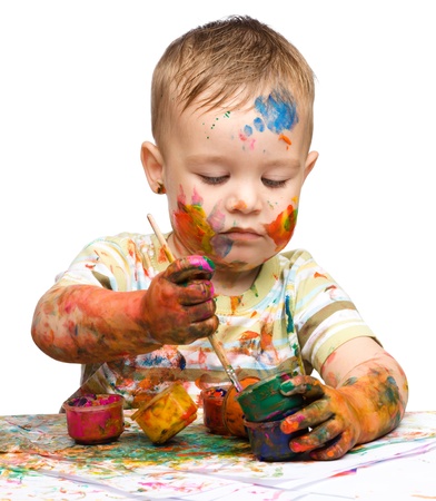 Portrait of a cute little boy messily playing with paints, isolated over whiteの写真素材