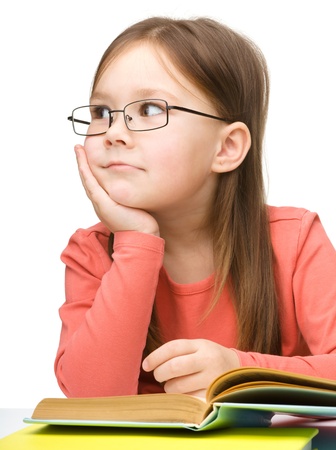 Cute little girl with black glasses is dreaming while reading book, isolated over whiteの写真素材