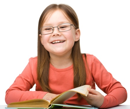 Cute cheerful little girl reading book wearing glasses, isolated over whiteの写真素材