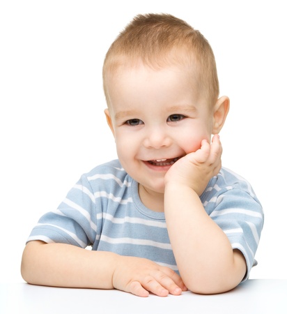 Portrait of a cute cheerful little boy, who is smiling while sitting at table, isolated over whiteの写真素材