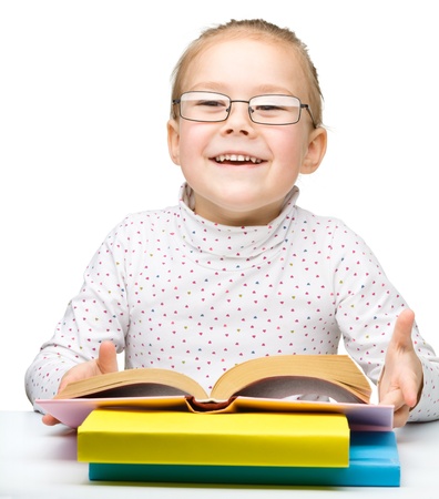Cute cheerful little girl reading book while wearing glasses, isolated over whiteの写真素材